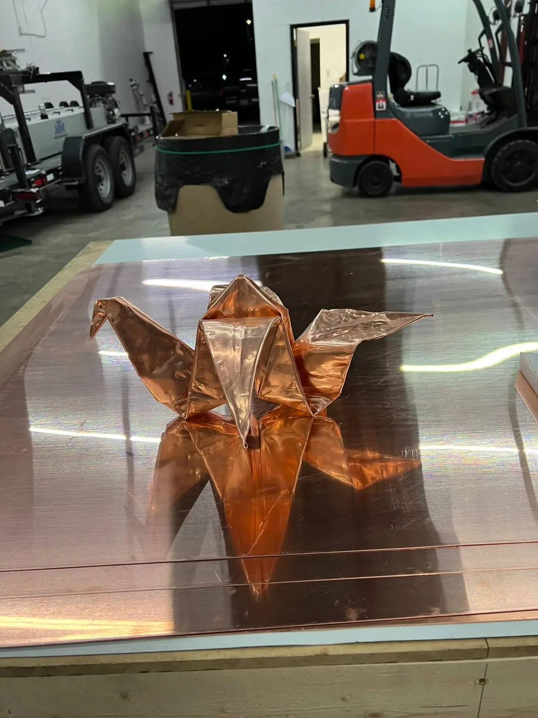 Folded copper crane standing on a sheet of bright copper in the shop
