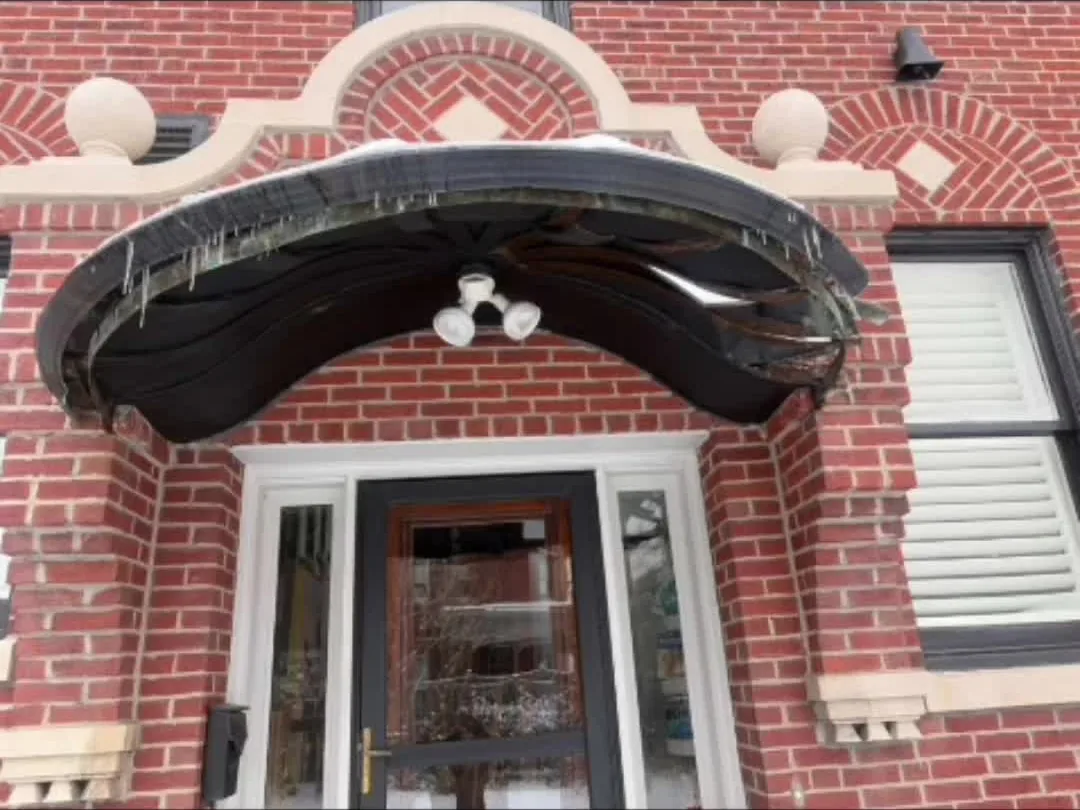 Curved copper hood over the front door of a red brick house, weathered to brown