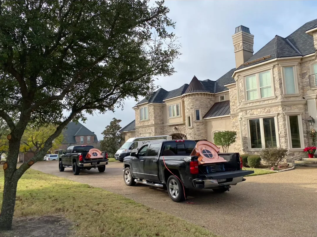 Two pickup trucks parked at the kerb of a large brick house on an installation day