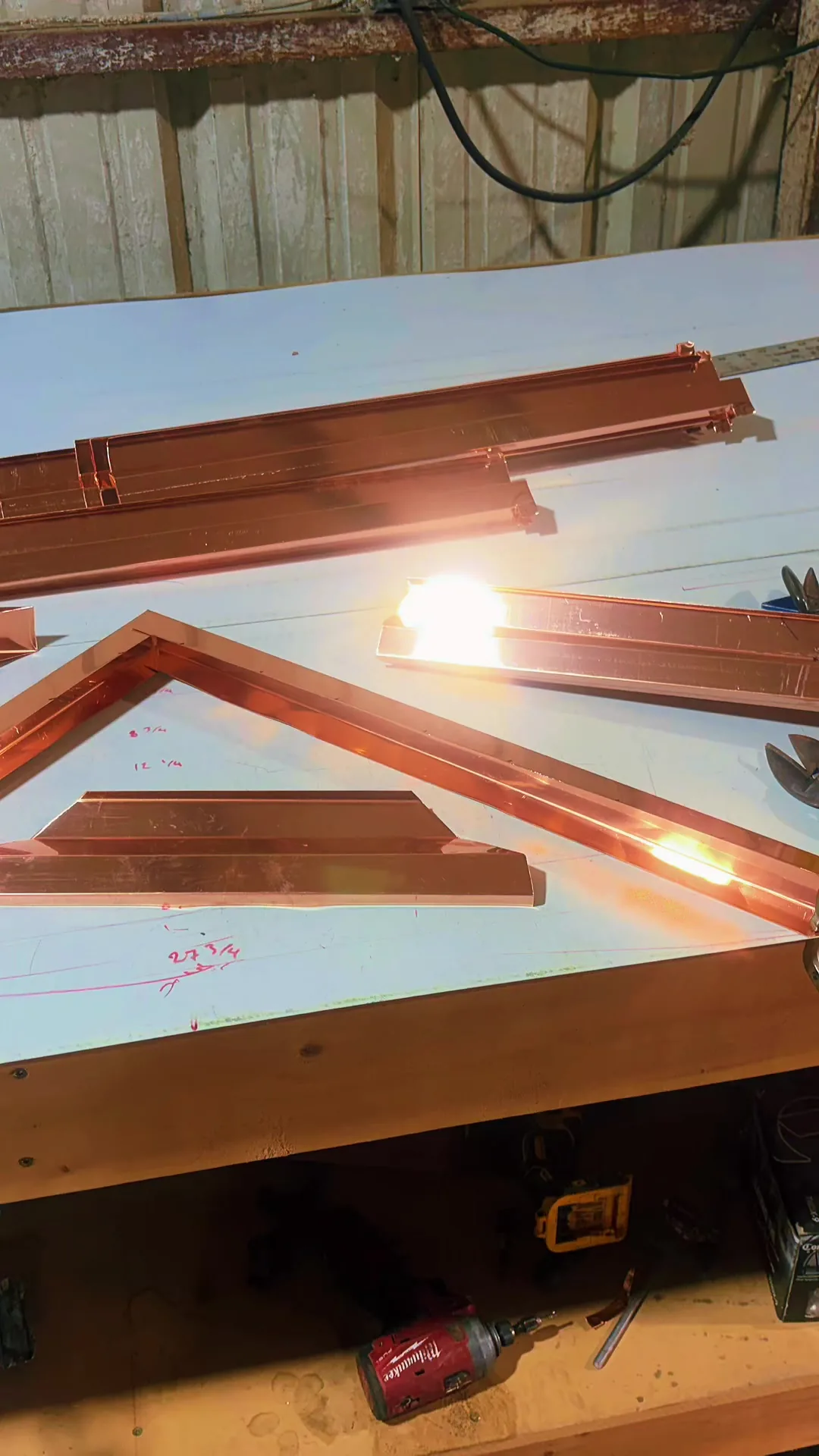 Lengths of copper trim and a mitred corner laid out on a workbench under the shop lights