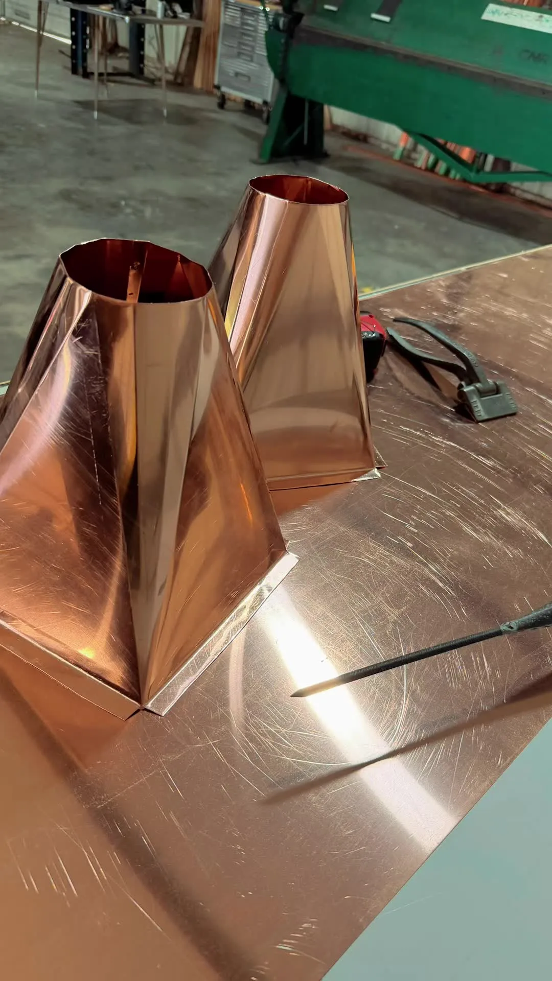 Two tapered copper transitions freshly formed on a bench in the shop, with the brake behind them