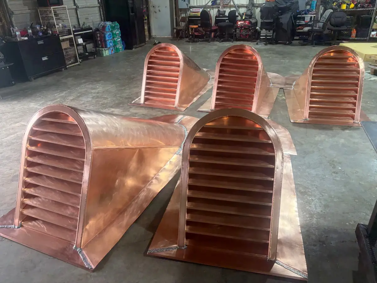 Arched copper dormer vents with horizontal louvers, laid out on the shop floor