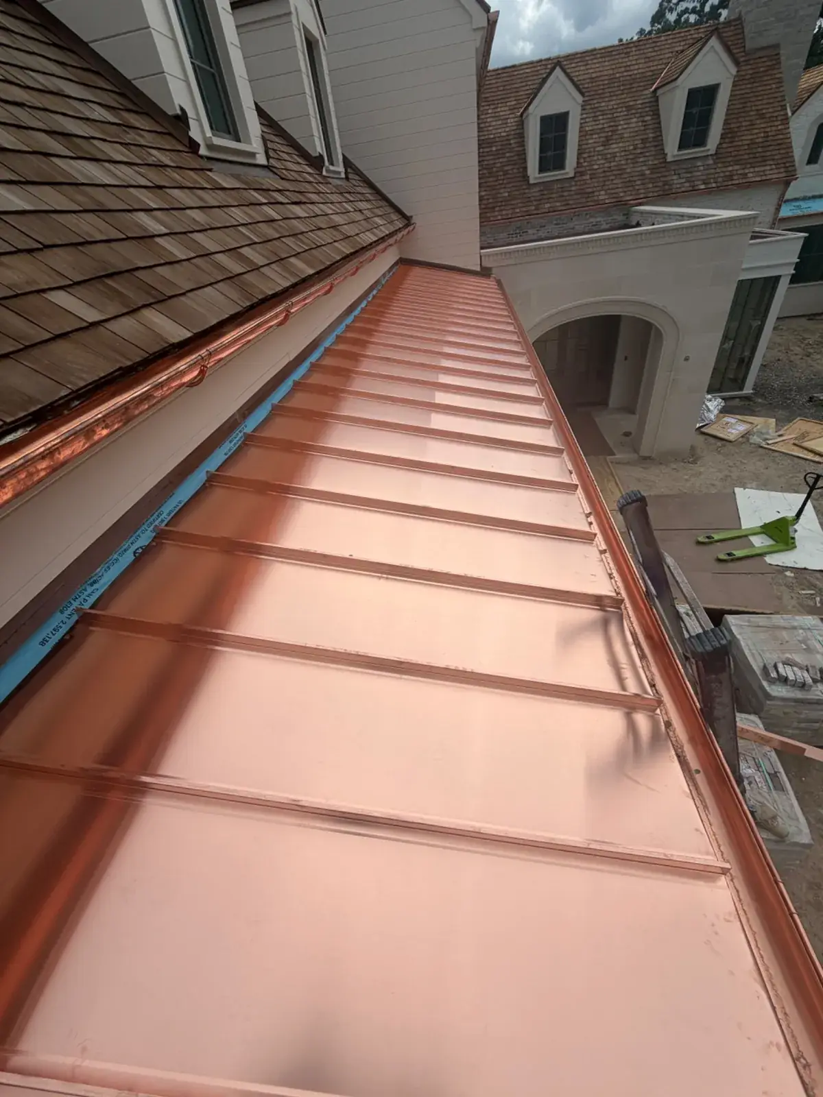 New copper liner running along a built-in gutter at the eave of a shingled roof, with dormers beyond