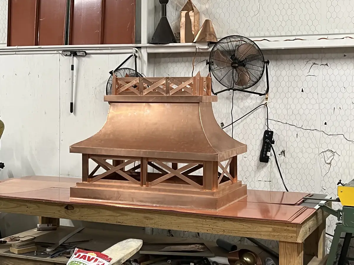 Copper chimney shroud with a flared pagoda roof and cross-braced side panels, on a shop bench