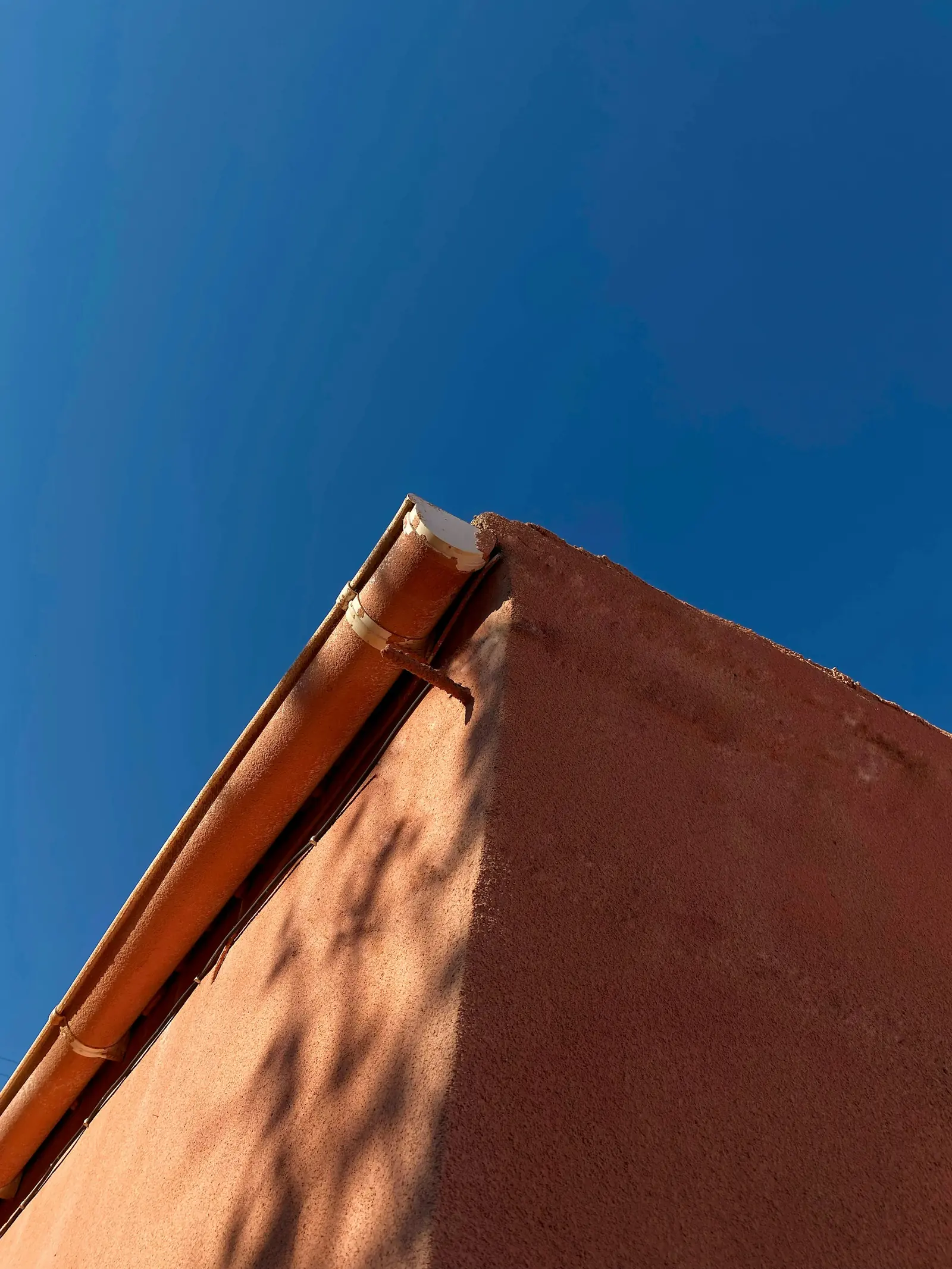 Copper gutter along the top of a terracotta wall, against a deep blue sky