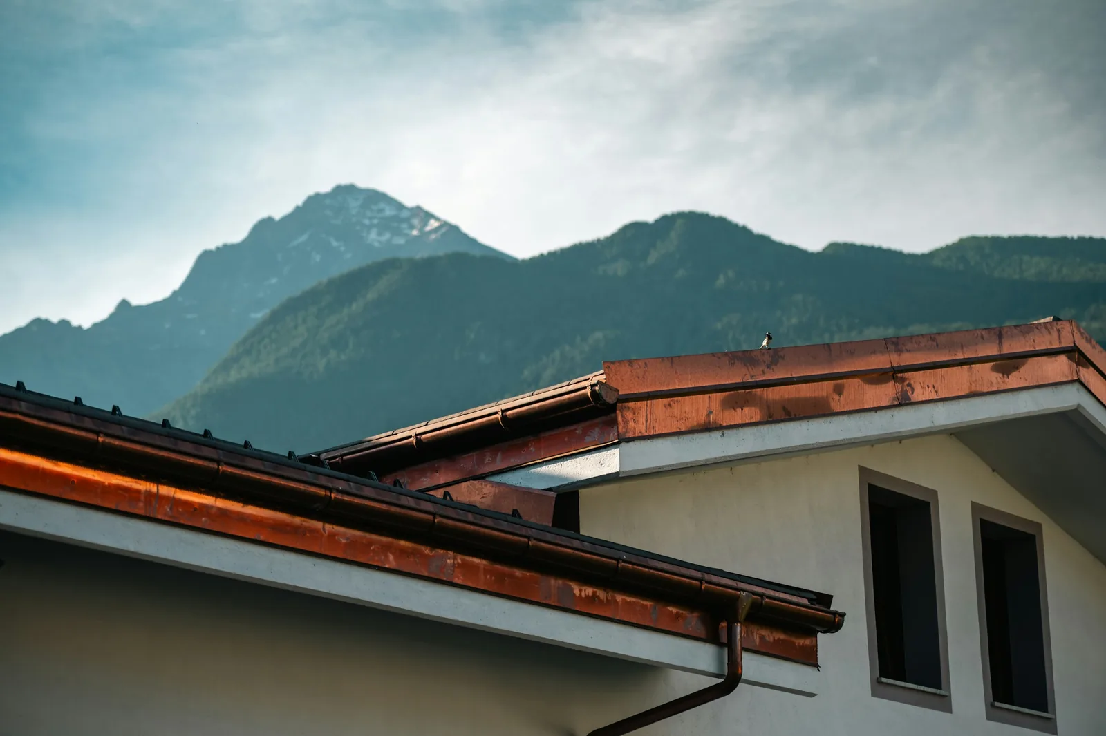 Copper gutters along the eaves of a white house, with mountains behind