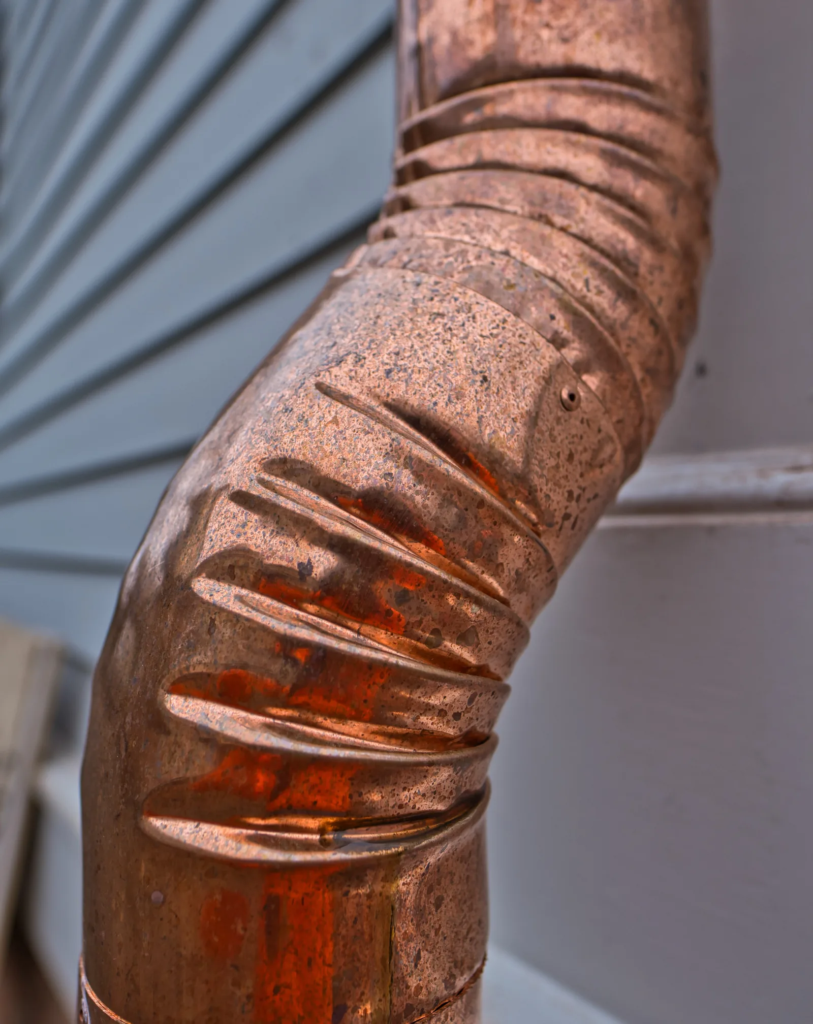 Crimped round copper elbow on a downspout beside grey siding