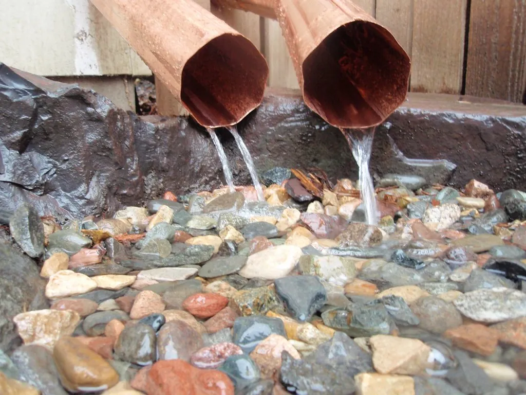 Two corrugated round copper downspouts emptying onto river stones