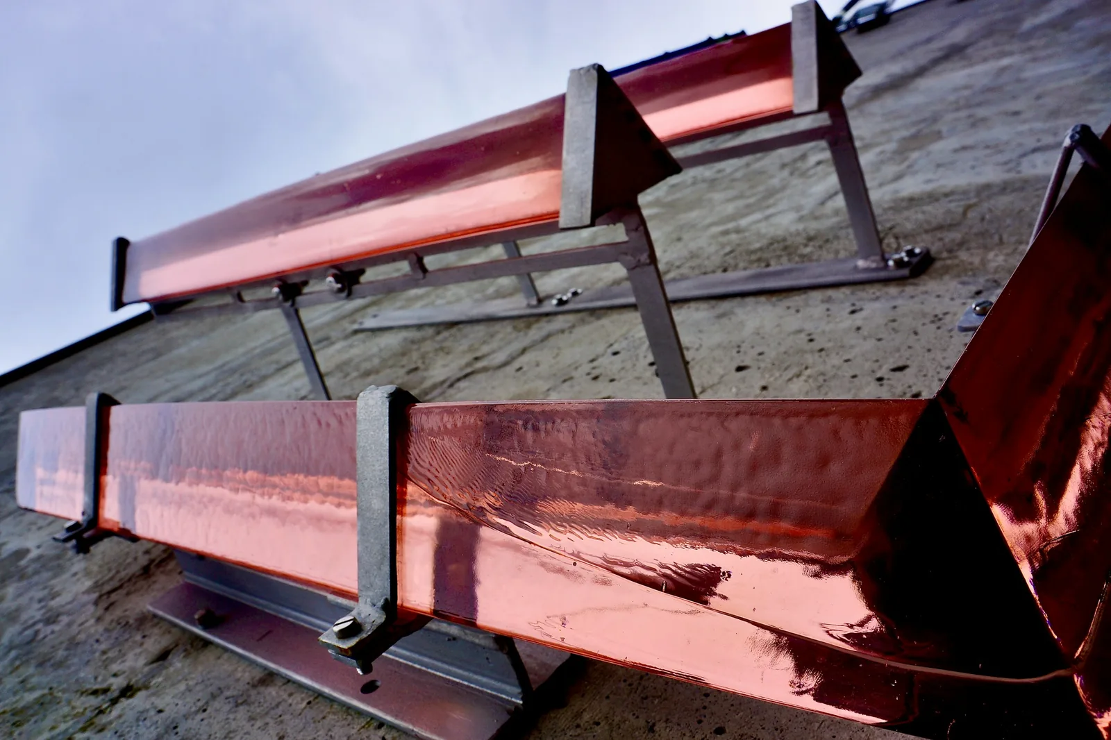 Lengths of copper gutter carried on metal hangers along a roof edge