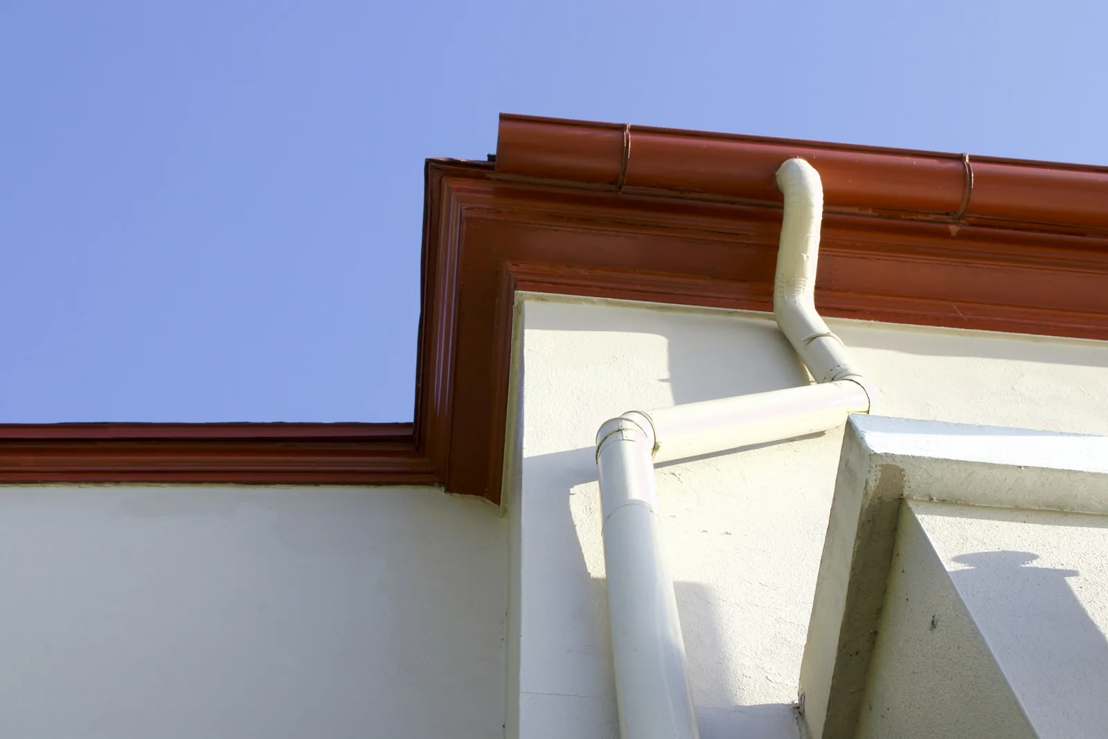 Copper gutter with a shaped front along the roof edge of a white building, against a blue sky