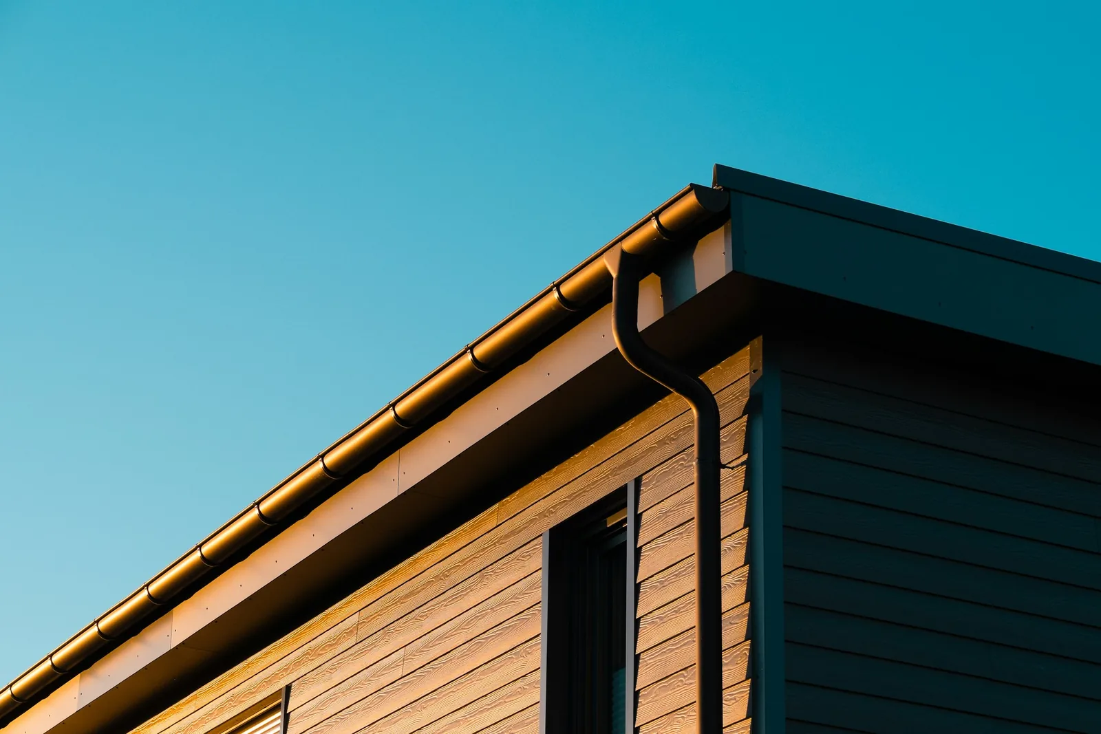 Metal gutter turning the corner of a modern building, against a clear sky